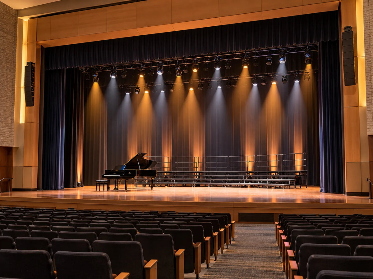 School performing arts auditorium with theatrical spotlights, a piano and choir risers